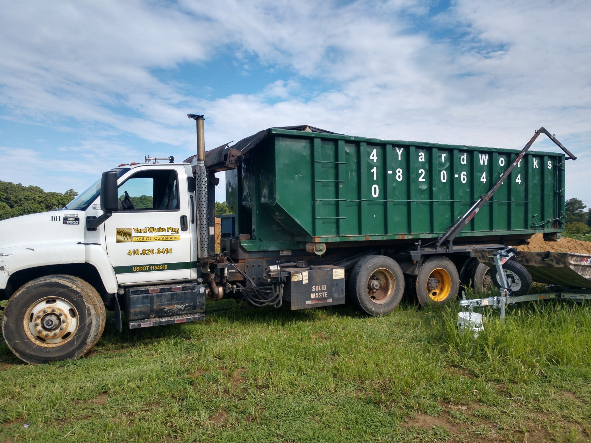 Yard Works Plus roll-off dumpster truck delivering a container
